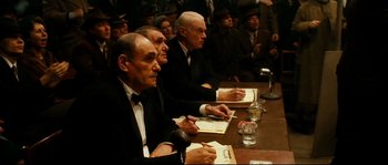Movie still from “La Vie En Rose” (2007), directed by Olivier Dahan – A group of men sitting at a table with papers in front of them; Medium shot, High angle