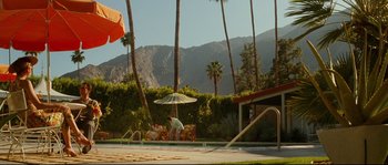 Movie still from “La Vie En Rose” (2007), directed by Olivier Dahan – A man standing under an umbrella near a swimming pool; Extreme Wide shot, High angle