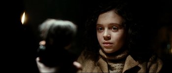 Movie still from “La Vie En Rose” (2007), directed by Olivier Dahan – A young girl looking at the camera in a dimly - lit room; Close Up shot, Over the shoulder angle
