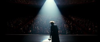 Movie still from “La Vie En Rose” (2007), directed by Olivier Dahan – A man standing on a stage in front of an audience; Extreme Wide shot, High angle