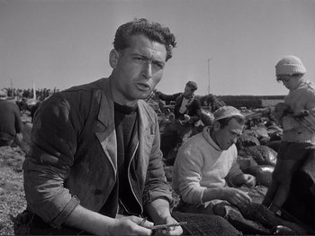Movie still from “The Earth Trembles” (1948), directed by Luchino Visconti – A black - and - white photo of a man holding a cell phone; Medium shot, Low angle