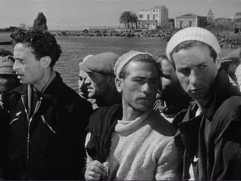 Movie still from “The Earth Trembles” (1948), directed by Luchino Visconti – A black and white photo of a group of men standing next to a body of water; Medium shot, Low angle
