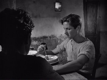 Movie still from “The Earth Trembles” (1948), directed by Luchino Visconti – A man sitting at a table with a bowl in front of him; Medium shot, Over the shoulder angle