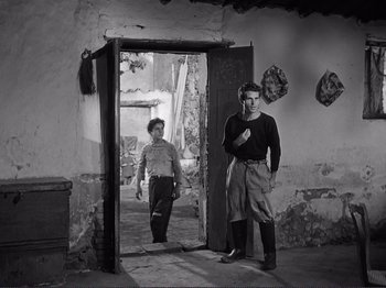Movie still from “The Earth Trembles” (1948), directed by Luchino Visconti – A man and a woman standing in front of an open door; Wide shot, Low angle