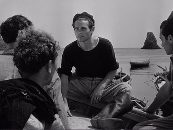 Movie still from “The Earth Trembles” (1948), directed by Luchino Visconti – A black and white photo of a man sitting on a boat; Medium shot, Over the shoulder angle