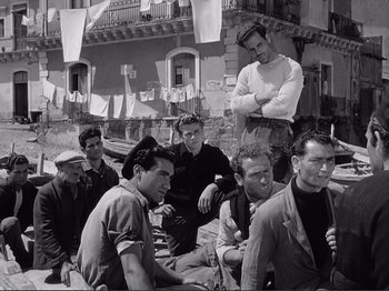 Movie still from “The Earth Trembles” (1948), directed by Luchino Visconti – A black and white photo of a group of men sitting on the ground; Medium shot, Low angle