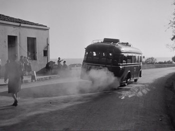 Movie still from “The Earth Trembles” (1948), directed by Luchino Visconti – An old black and white photo of a bus driving down the street; Wide shot, Low angle
