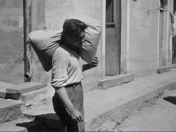 Movie still from “The Earth Trembles” (1948), directed by Luchino Visconti – A man carrying a large bag on his head; Wide shot, Low angle