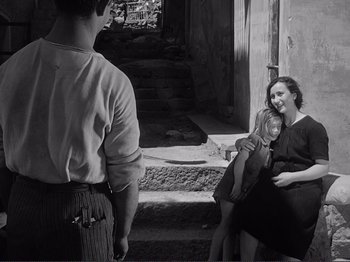 Movie still from “The Earth Trembles” (1948), directed by Luchino Visconti – Two women and a man sitting on steps; Medium shot, Over the shoulder angle
