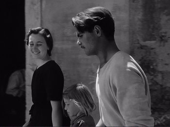 Movie still from “The Earth Trembles” (1948), directed by Luchino Visconti – A black and white photo of two people and a child; Medium shot, Over the shoulder angle