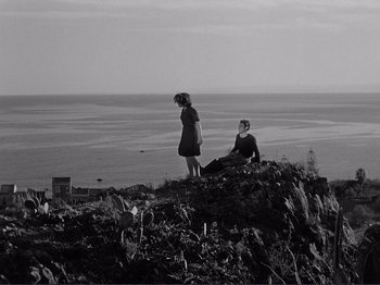 Movie still from “The Earth Trembles” (1948), directed by Luchino Visconti – Two people sitting on top of a hill near the ocean; Extreme Wide shot, High angle