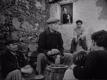 Movie still from “The Earth Trembles” (1948), directed by Luchino Visconti – An old man sitting on the ground in front of a group of people; Medium shot, Low angle