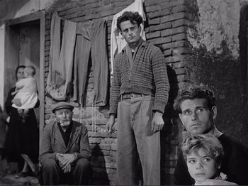 Movie still from “The Earth Trembles” (1948), directed by Luchino Visconti – A group of people standing in front of a brick wall; Wide shot, Low angle