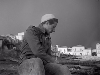 Movie still from “The Earth Trembles” (1948), directed by Luchino Visconti – A black and white photo of a man sitting on the ground; Medium shot, Low angle