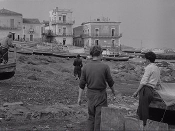 Movie still from “The Earth Trembles” (1948), directed by Luchino Visconti – A black and white photo of people standing on the beach; Wide shot, Low angle