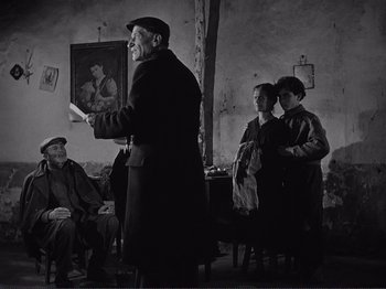 Movie still from “The Earth Trembles” (1948), directed by Luchino Visconti – An old man standing in front of a group of people; Medium shot, Low angle