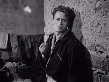 Movie still from “The Earth Trembles” (1948), directed by Luchino Visconti – A black and white photo of a man smoking a cigarette; Medium shot, Low angle