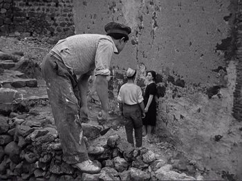 Movie still from “The Earth Trembles” (1948), directed by Luchino Visconti – An old photo of a man and two women; Wide shot, Low angle