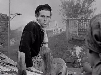 Movie still from “The Earth Trembles” (1948), directed by Luchino Visconti – A man sitting on top of a wooden post; Medium shot, Low angle