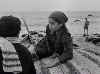 Movie still from “The Earth Trembles” (1948), directed by Luchino Visconti – A young girl sitting on a dock next to the ocean; Medium shot, High angle