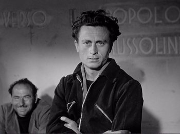 Movie still from “The Earth Trembles” (1948), directed by Luchino Visconti – A black and white photo of a man with his arms crossed; Medium shot, Low angle