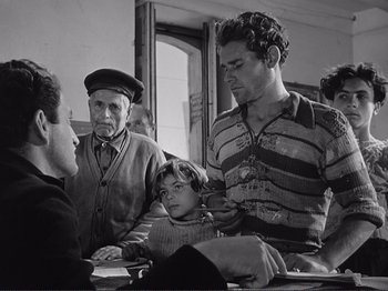 Movie still from “The Earth Trembles” (1948), directed by Luchino Visconti – An old man and a young boy are sitting at a table with other people; Medium shot, Over the shoulder angle