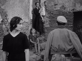 Movie still from “The Earth Trembles” (1948), directed by Luchino Visconti – A group of people standing on steps near a brick wall; Medium shot, Over the shoulder angle