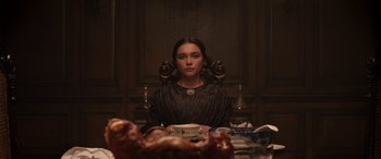 Movie still from “Lady Macbeth” (2016), directed by William Oldroyd – A woman sitting at a table with a plate of food in front of her face; Medium shot, Over the shoulder angle