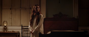 Movie still from “Lady Macbeth” (2016), directed by William Oldroyd – A woman standing in front of a piano in a room; Medium shot, Over the shoulder angle