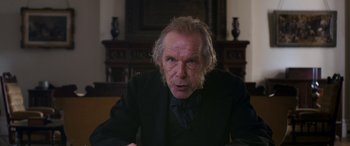 Movie still from “Lady Macbeth” (2016), directed by William Oldroyd – An older man in a black suit is sitting in front of a fireplace; Close Up shot, Over the shoulder angle