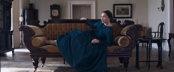 Movie still from “Lady Macbeth” (2016), directed by William Oldroyd – A woman in a blue dress sitting on a couch in a living room; Wide shot, Low angle