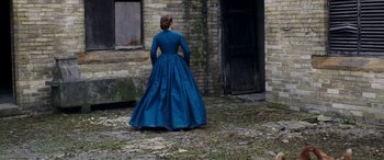 Movie still from “Lady Macbeth” (2016), directed by William Oldroyd – A woman in a blue dress standing in front of a brick building; Wide shot, Over the shoulder angle
