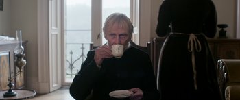 Movie still from “Lady Macbeth” (2016), directed by William Oldroyd – An older man drinking a cup of coffee; Medium shot, Low angle