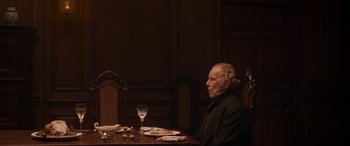 Movie still from “Lady Macbeth” (2016), directed by William Oldroyd – An older man sitting at a table with a plate of food; Medium shot, Over the shoulder angle