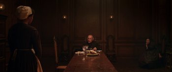 Movie still from “Lady Macbeth” (2016), directed by William Oldroyd – An older man sitting at a table with a plate of food; Wide shot, High angle