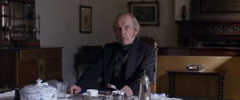 Movie still from “Lady Macbeth” (2016), directed by William Oldroyd – An older man sitting at a table with a knife in his hand; Medium shot, Over the shoulder angle