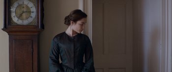 Movie still from “Lady Macbeth” (2016), directed by William Oldroyd – A woman in a black dress standing next to a door; Medium shot, Over the shoulder angle