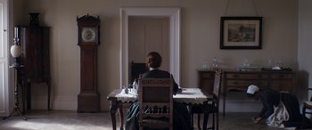 Movie still from “Lady Macbeth” (2016), directed by William Oldroyd – A woman sitting at a table in front of an open door; Wide shot, High angle