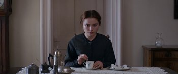 Movie still from “Lady Macbeth” (2016), directed by William Oldroyd – A woman sitting at a table with a cup of coffee; Medium shot, Over the shoulder angle