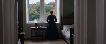 Movie still from “Lady Macbeth” (2016), directed by William Oldroyd – A woman standing in front of a window looking out at trees; Wide shot, High angle