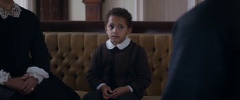 Movie still from “Lady Macbeth” (2016), directed by William Oldroyd – A young boy sitting on a couch looking at the camera; Close Up shot, High angle
