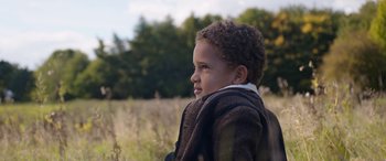 Movie still from “Lady Macbeth” (2016), directed by William Oldroyd – A little boy sitting in a field of tall grass; Close Up shot, Over the shoulder angle