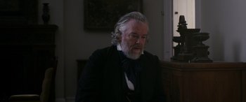 Movie still from “Lady Macbeth” (2016), directed by William Oldroyd – An older man with a long gray beard wearing a black suit; Close Up shot, Over the shoulder angle