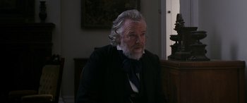 Movie still from “Lady Macbeth” (2016), directed by William Oldroyd – An older man in a suit and tie sitting in a chair; Close Up shot, Over the shoulder angle