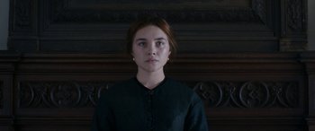 Movie still from “Lady Macbeth” (2016), directed by William Oldroyd – A young woman in a black shirt is standing in front of a wall; Close Up shot, Over the shoulder angle