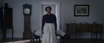 Movie still from “Lady Macbeth” (2016), directed by William Oldroyd – A woman standing in front of a dining room table; Medium shot, Over the shoulder angle