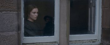 Movie still from “Lady Macbeth” (2016), directed by William Oldroyd – A woman looking out of a window at a person behind a window; Medium shot, Over the shoulder angle