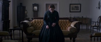 Movie still from “Lady Macbeth” (2016), directed by William Oldroyd – A woman in a black dress standing in front of a couch; Medium shot, Low angle