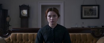 Movie still from “Lady Macbeth” (2016), directed by William Oldroyd – A woman sitting on a couch in front of a window; Medium shot, Over the shoulder angle