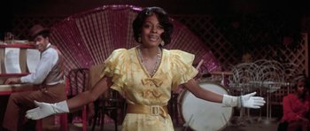 Movie still from “Lady Sings the Blues” (1972), directed by Sidney J. Furie – A woman in a yellow dress is standing in front of a drum set; Medium shot, Low angle